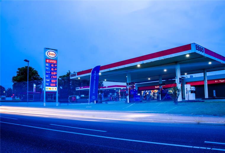 Auto fahren am Morgen an einer Tankstelle vorbei an deren Preistafel die aktuellen Literpreise für Kraftstoff angezeigt werden. 