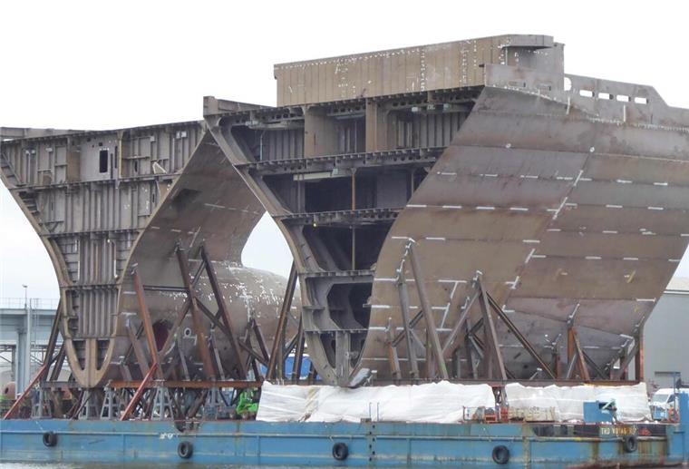 Zwei Schiffssektionen stehen auf einer Werft. 
