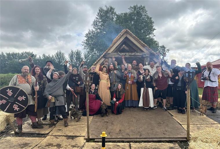 Menschen im Wikinger-Outfit vor einer Wikinger-Hütte.