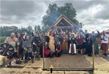 Menschen im Wikinger-Outfit vor einer Wikinger-Hütte.