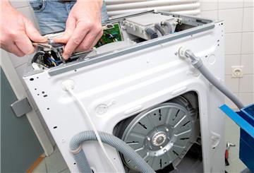 Ein Mann repariert eine Waschmaschine. Die Verbraucherzentrale warnt vor unseriösen Reparaturdiensten.