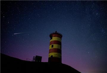 Eine Sternschnuppe leuchtet über der Nordsee am Nachthimmel über dem Pilsumer Leuchtturm. 