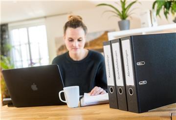 Eine Frau sitzt am Schreibtisch vor ihrem Laptop und Ordnern