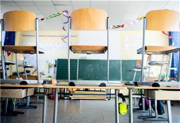 Mehrere Stühle stehen in einem leeren Klassenzimmer auf den Tischen. Im Hintergrund ist die Tafel zu sehen.