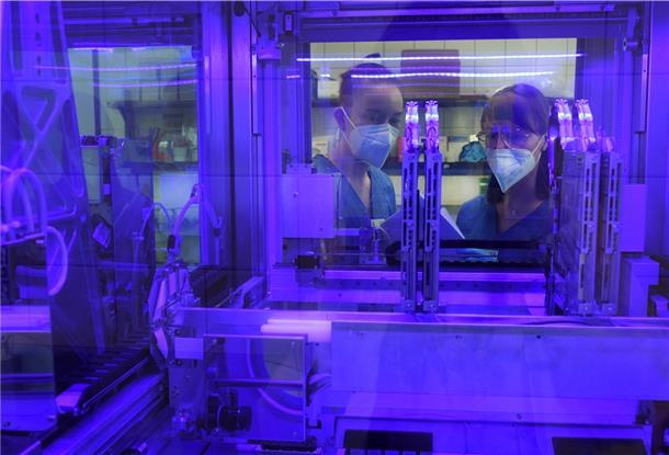 Symbolbild: An einem blau beleuchteten Vollautomaten im PCR-Labor beobachten zwei Medizinisch technische Laborassistentinnen die Bearbeitung von PCR-Tests, die innerhalb von drei Stunden in dem Automaten analysiert werden.Foto: Waltraud Grubitzsch/dpa