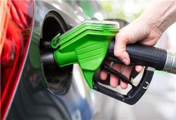 Eine Frau hält an einer Tankstelle an einer Zapfsäule eine Zapfpistole in der Hand und betankt ein Auto.