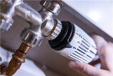  Eine Person dreht am Thermostat einer Heizung. 