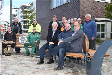 Testsitzung am Neuen Hafen im Kreise von Mitarbeitern der Raumwerkerei: Auf der Fischbank im Vordergrund sitzen (von links) Stadtrat Uwe Parpart, Raumwerkerei-Architekt Esfandiar Dilmaghani und Günther Kerchner, Vorstand der Stiftung Inklusive Stadt. Im Hintergrund steht die neue Seestadtbank.