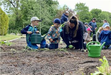 Thies (4) und Bennet (4) arbeiten in Teamwork. Einer gießt Wasser ins Loch, der andere setzt die Pflanze hinein. Erzieherin Jana Steffens unterstützt die beiden Acker-Racker.