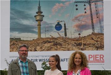Torsten Tingler freut sich zusammen mit Katharina Perokovic und Nicole Halves-Volmer von der Erlebnis Bremerhaven GmbH über das Großflächenplakat seines Gewinnerbildes an dem Standort Columbusstraße, Höhe Hochschule Haus C.