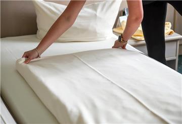 Eine Mitarbeiterin eines Hotels streicht eine Bettdecke in einem Hotelzimmer glatt.