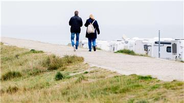 Touristen gehen bei trübem Wetter auf einem Deich vor der Nordsee entlang.