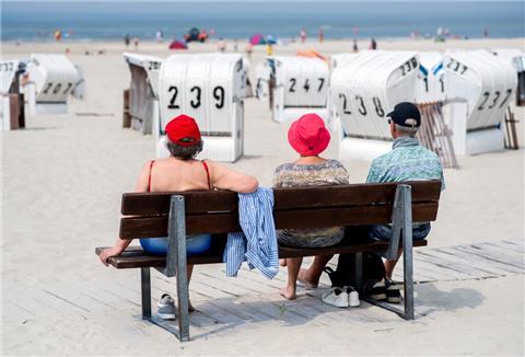 Drei Touristen sitzen bei sonnigem Wetter auf einer Bank an einem Strand .