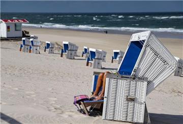 Eine Strandbesucherin liest bei sommerlichem Wetter ein Buch in einem Strandkorb