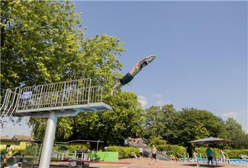 Ein Sprungturm im Freibad Grünhöfe in Bremerhaven, von dem ein Mann in Badeshorts gestreckt abspringt.