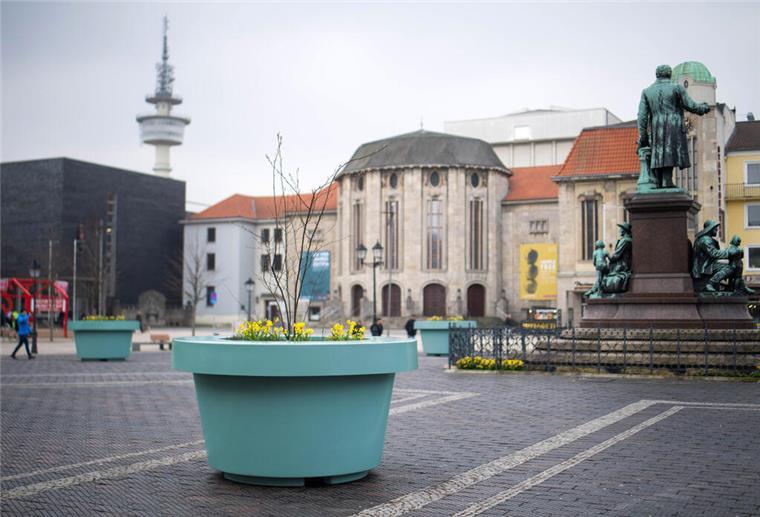 Ein türkisfarbener Kübel ist auf einem öffentlichen Platz zu sehen. 