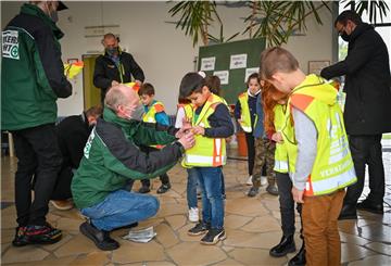Übergabe der Kinderwarnwesten im Foyer der Goetheschule: Gerhard Thielbar (Verkehrswacht Bremen-Nord) streift Loai eine Weste über. Links ist Tim Thielbar zu sehen, rechts Frank Stickel von der Gewoba. 
