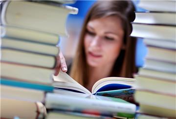 Eine junge Frau liest an einem Tisch voller Bücher