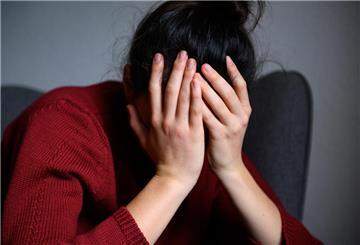  Eine Frau sitzt mit dem Kopf in den Händen auf einem Stuhl. 