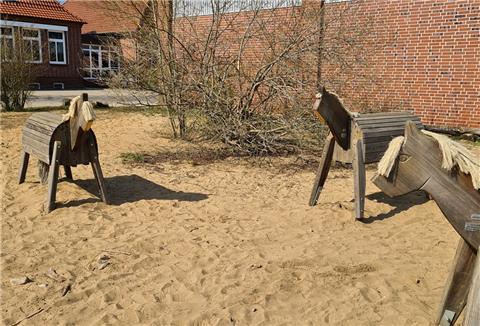 Drei Holzpferde stehen im Sand.