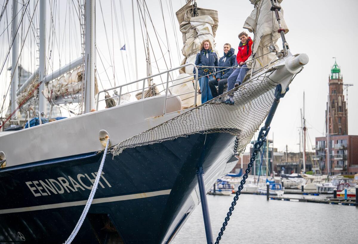 Schule unter Segeln: Diese Jugendlichen lernen mitten auf dem Atlantik Zwei junge Frauen und ein junger Mann stehen vorne auf einem Schiff.