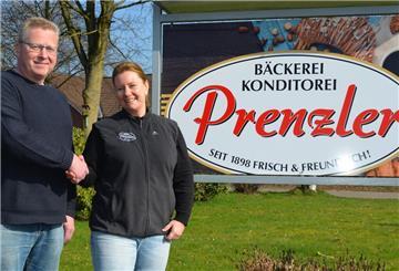 Zwei Menschen geben sich die Hand und stehen vor dem Bäckerei Prenzler Schild.