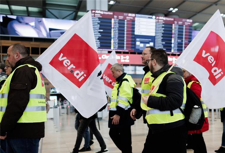 ARCHIV - 14.03.2024, Brandenburg, Schönefeld: Mitarbeiter des Luftsicherheitspersonals demonstrieren mit Fahnen der Dienstleistungsgewerkschaft Verdi in der Abflughalle im Terminal 1 des Flughafens BER. (zu dpa: «67.000 Passagiere betroffen - Warnstreik am BER läuft») Foto: Carsten Koall/dpa +++ dpa-Bildfunk +++