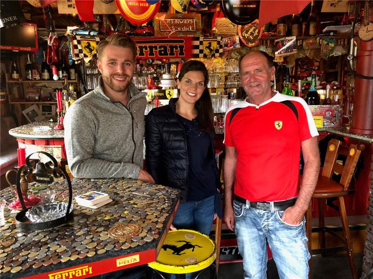 Verrückt nach Meer? Verrückt nach Ferrari! Das TV-Protagonisten-Pärchen der ARD-Serie, Jonas Dülberg und Indra Uihlein, haben wie schon so viele Gäste Münzen auf den Tisch der Kultkneipe geklebt. Inhaber ist Hans „Hansi“ Sauerbrei (rechts). Bayerischer Rundfunk/Farah M’haimdat.
