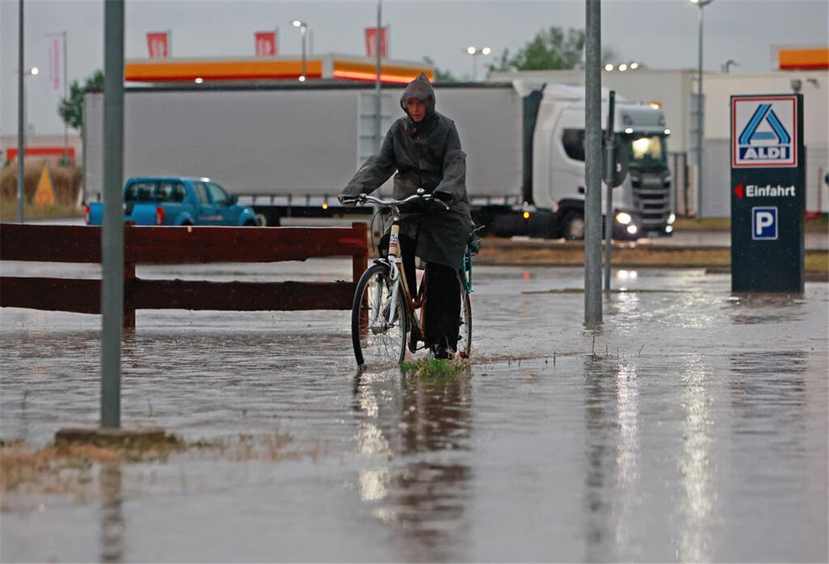  Eine Frau fährt nach einem Unwetter mit Starkregen mit ihrem Fahrrad über eine überflutete Straße in einem Gewerbegebiet. 