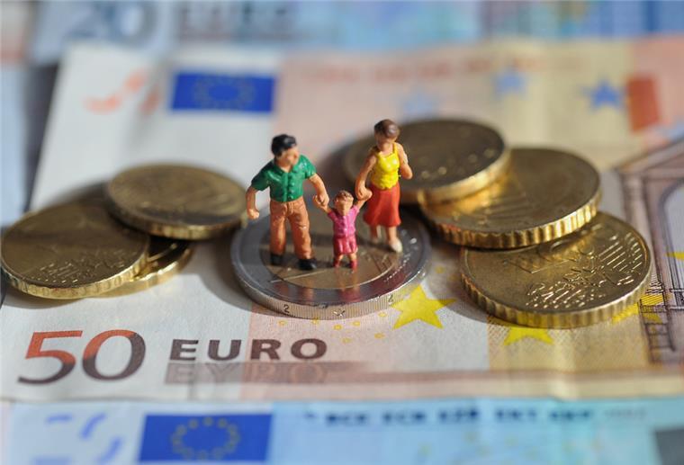 Ein Paar mit einem Kind steht auf einer Zwei-Euro-Münze, die auf einem 50-Euro-Schein liegt.