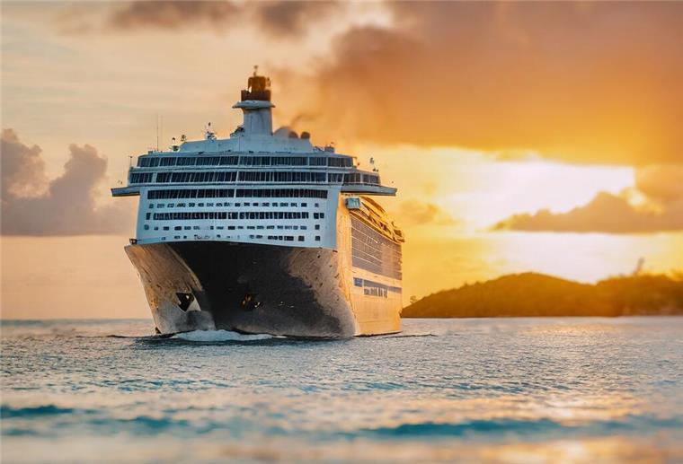 Ein Kreuzfahrtschiff ist auf dem Wasser unterwegs. Im Hintergrund ist ein Sonnenuntergang zu sehen.