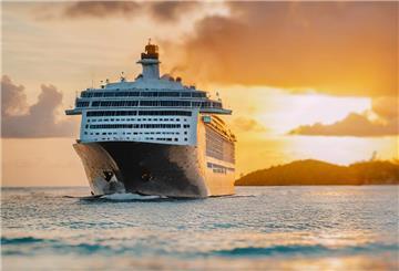 Ein Kreuzfahrtschiff ist auf dem Wasser unterwegs. Im Hintergrund ist ein Sonnenuntergang zu sehen.