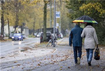  Passanten mit Regenschirm sind im Regen auf dem Gehweg unterwegs. 