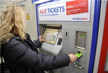 Eine blonde, junge Frau in einer dicken, schwarzen Jacke steckt ihre grüne BOB-Fahrkarte in einen Fahrkartenautomaten der Nordwestbahn und bedient das Display.