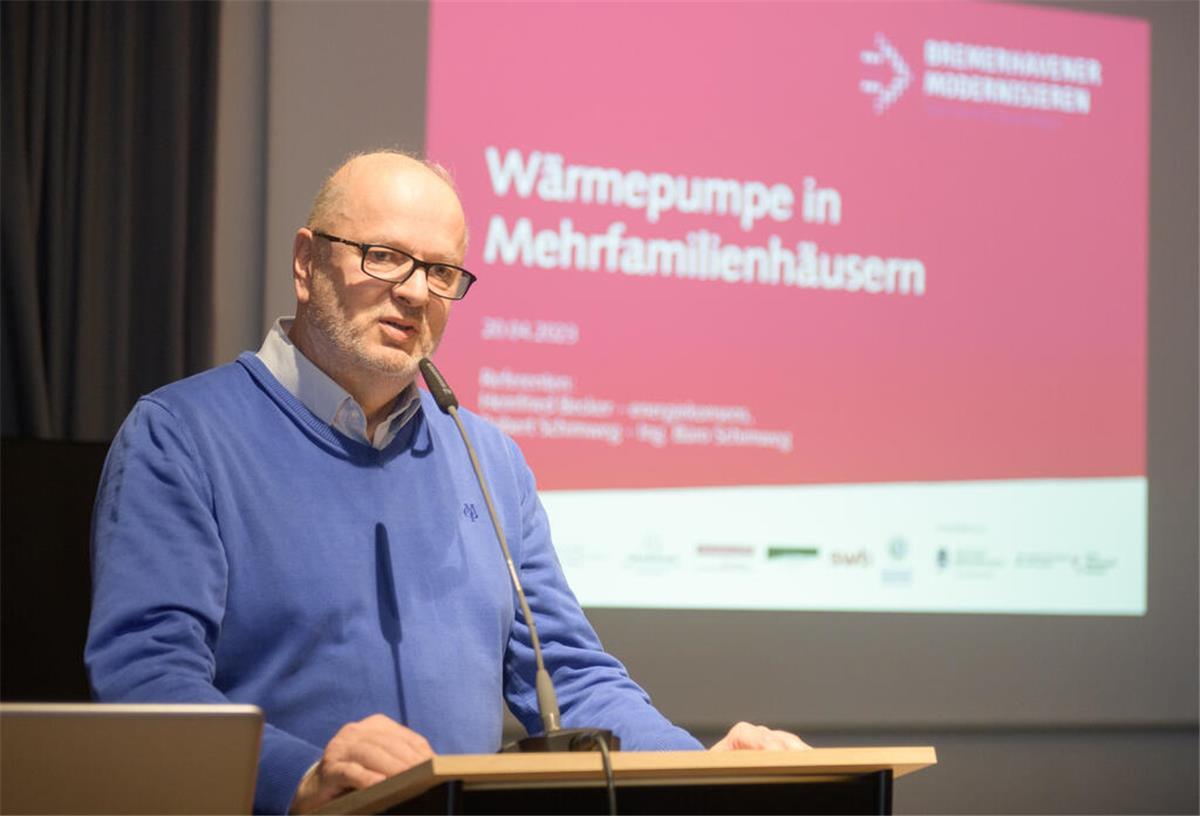 Wärmepumpenwochen in Bremerhaven und Bremen Ein Referent hält einen Vortrag zum Thema "Wärmepumpen in Mehrfamilienhäusern". Das Thema ist im Hintergrund auf einer Leinwand zu sehen.