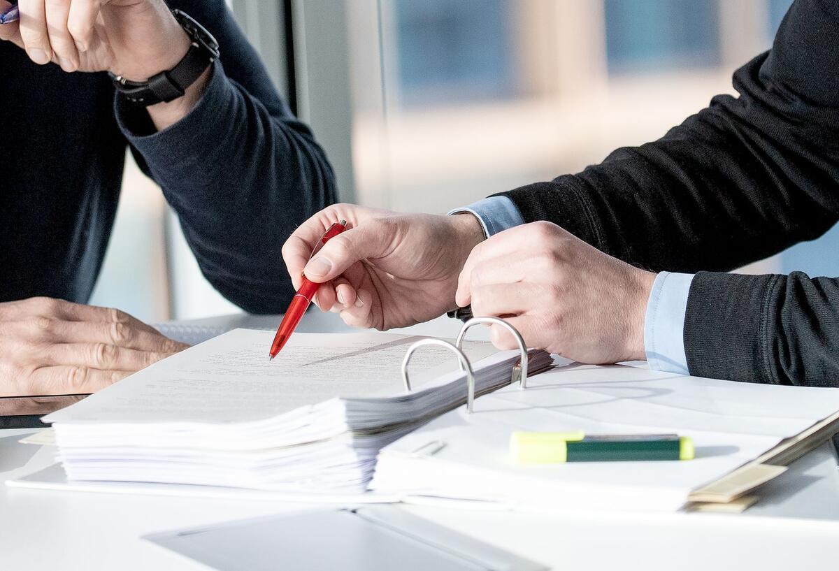 Arbeitsunfall, oder nicht? Wann greift die gesetzliche Unfallversicherung Zwei Menschen sitzen über einem Ordner mit Papieren.