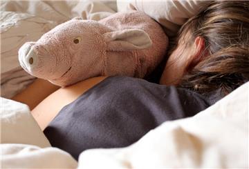 Eine Frau liegt am mit einem Kuscheltier im Bett. Was zart klingt, hat oft ernste Botschaften: Viele Schlaflieder handeln von Angst, Verlust oder Fürsorge. In manchen Kulturen bekommen sogar Schafe ein Wiegenlied gesungen.