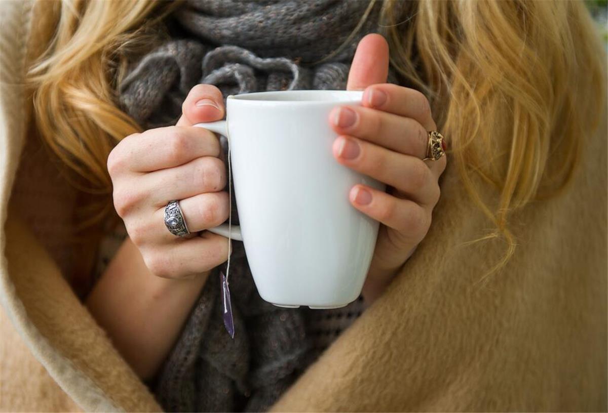 Eine Frau hält eine weiße Tasse mit einem Teebeutel in der Hand.