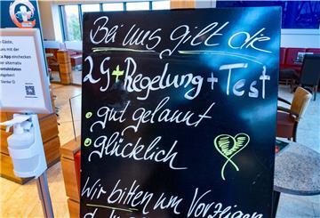 Ein Schild mit dem Schriftzug "2G+Regelung+Test - gut gelaunt - glücklich" steht vor einem Eiscafé