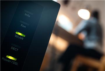 Eine Frau arbeitet im Home Office. Im Vordergrund steht ein Router, auf dem die LED für W-Lan und DSL leuchten.
