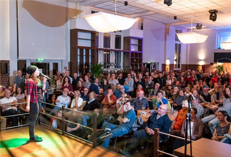Eine Frau steht auf einer Bühne. Vor ihr sind zahlreiche Menschen im Publikum.