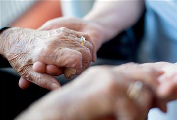 Eine Seniorin hält sich mit ihren Händen an den Händen einer Pflegekraft fest. 