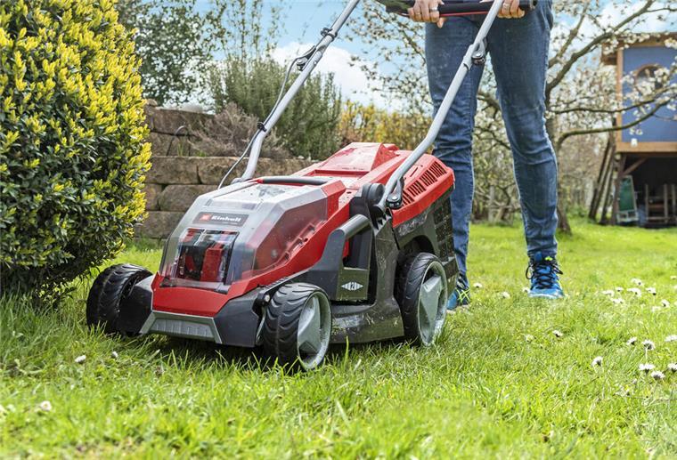 Sicher Rasen mähen nach Regen: Die wichtigsten Tipps Ein roter Rasenmäher mäht einen Garten.