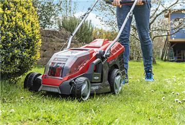 Ein roter Rasenmäher mäht einen Garten.
