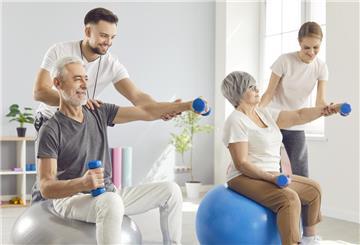 Glückliche Senioren bei einer Reha mit zwei Fitnessexperten. Wer eine Reha plant, hat Mitspracherecht – bei Ort, Zeitpunkt und Klinik. Wichtig ist, dies direkt im Antrag klar anzugeben.