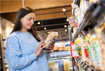 Eine Frau im Supermarkt hält eine Packung in der Hand. Wer es schlau anstellt, kann im Supermarkt jede Menge bares Geld sparen.