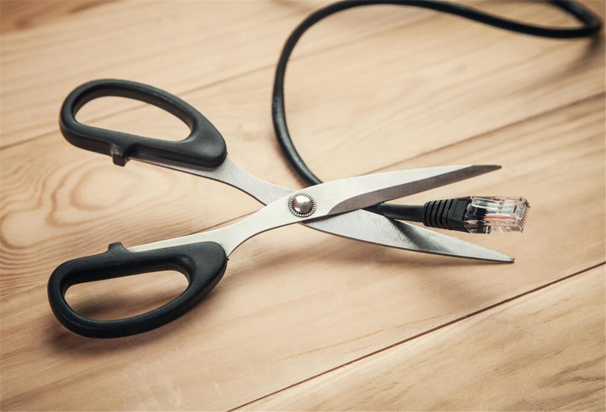 Eine Schere schneidet ein DSL-Kabel durch, das auf einem Tisch liegt. Wer noch über DSL im Internet surft, muss bald handeln. Millionen Deutsche sind betroffen.