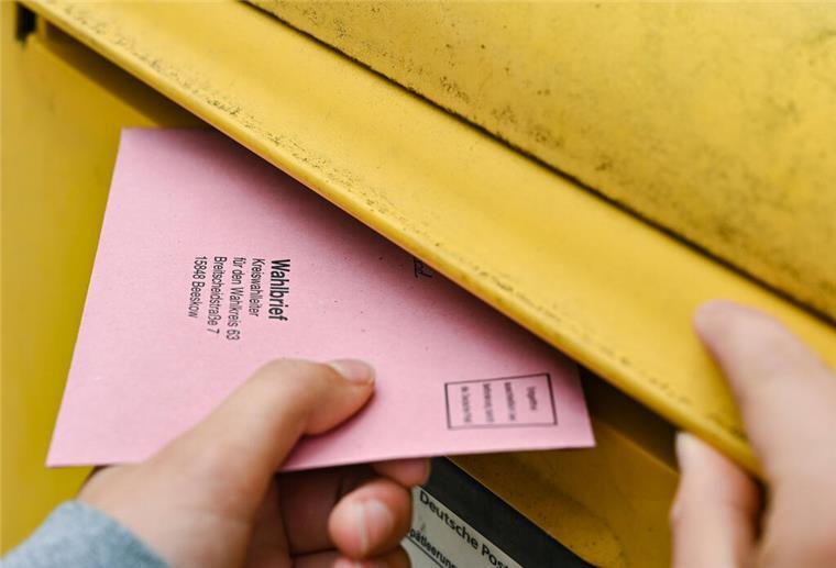 Eine Person wirft ihre Briefwahlunterlagen in einen Postkasten der Deutschen Post.