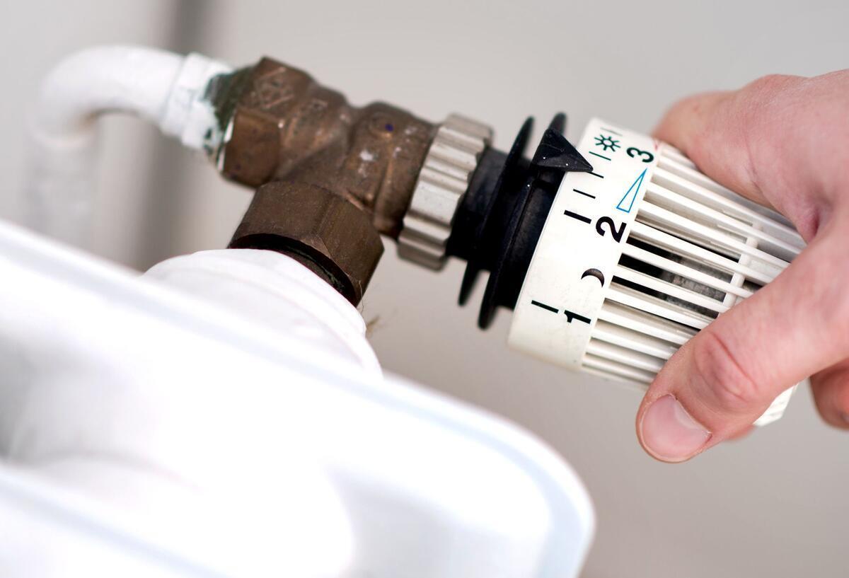 Symboldbild für Richtig heizen und Geld sparen: Ein Mann dreht das Thermostat an einem Heizkörper auf.