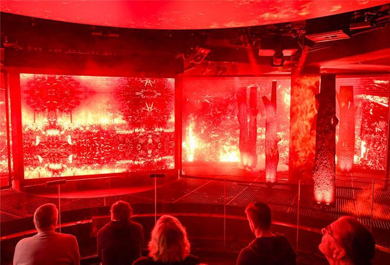 Nach 3 Monaten Verzögerung: Klimahaus Bremerhaven startet Extremwetter-Ausstellung Menschen schauen auf große Bildschirme, auf denen Extremwetter-Phänomene zu sehen sind.